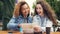 Excited girls tourists are checking city map and looking around then laughing sitting in street cafe in foreign country