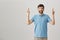 Excited happy good-looking male with beard standing with lifted hands and crossed fingers over gray background, desiring