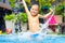 Excited happy kid boy jumping in pool, water fun