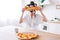 Excited happy young woman in kitchen plaing with pizza slices. Cover eyes with food. Carefree housekeeper very playful