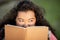 Excited hispanic student lady holding book reading outdoors, portrait