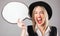 Excited joyful screaming woman in black hat and red lips holding emoty white spech buble