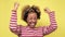 Excited joyous african woman raises clenched fists, on yellow background