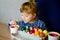 Excited little toddler girl coloring eggs for Easter. Child looking surprised at colored egg hoarding and celebrating