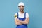 Excited man in coveralls protective helmet hardhat hold paint brush isolated on blue wall background. Instruments