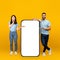 Excited millennial arab couple showing smartphone blank screen on yellow background, mockup for mobile app or website