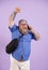 Excited obese man with bag talks on smartphone raising up fist on purple background