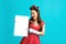 Excited pinup retro style woman pointing at empty advertising banner with copy space on blue studio background, mockup