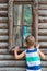 Excited preschooler boy looks into window of log house