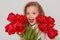 Excited schoolgirl with red tulips in hands, looking at camera with widely opened mouth, having fun alone, being happy to get such