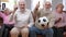 Excited senior men cheering watching football match as bored women sitting on couch with dissatisfied facial expression