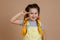 Excited shining small girl with yellow kanekalon pigtails, smiling with missing tooth holding finger by temple in yellow