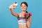 Excited sports woman in white top making selfie exercising with dumbbell, monitoring her indicators on smartwatch through app on