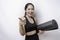 Excited sporty Asian woman wearing sportswear pointing at the camera while carrying yoga mat, isolated by white background