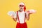 Excited surprised elderly man in santa claus hat and stylish sunglasses holding giftbox and dollar banknotes, holiday bonuses