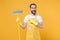 Excited surprised young man househusband in apron rubber gloves doing housework isolated on yellow wall background