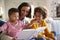 Excited toddler boy sitting on his motherï¿½s knee reading a book in the living room with his older sister, close up