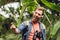 Excited traveler with backpack and binoculars listening music in headphones and singing in tropical forest.