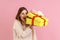 Excited young adult blond woman looking inside yellow present box, being interested what inside.