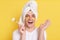 Excited young adult man wrapped towel on head doing morning cosmetology procedures, holding massage with roller, being happy,