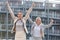 Excited young businesswomen gesturing thumbs up against office building