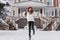 Excited young fashionable woman having fun, jumping in snow on street in winter time. Long brunette hair, red hat