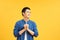 Excited young ma laughing out loud and clasping hands while standing against yellow background