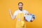 Excited young man househusband in apron hold basket with clean clothes doing housework isolated on yellow background