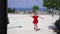 Excited young slim beautiful woman in red dress and sunglasses running spinning in sunlight on Mediterranean summer