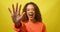 Excited young woman holds up hand, high five close up, yellow studio shoot