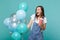 Excited young woman keeping mouth open, hold plastic cup of cola or soda, celebrating with colorful air balloons