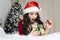 Excited young woman opening a Christmas gift. Cute girl in a Santa Claus costume unleashes a ribbon on a new year gift lying on