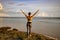 Excited young woman raising arms at the beach in front of the ocean. View from back. Freedom and energy. Bali, Indonesia