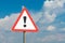 Exclamation mark on a road sign with a white nameplate background sky with clouds