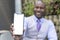 Executive black man showing a smartphone with a blank screen. He is wearing a medical mask and formal wear. Selective focus. Space