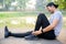 Exercise Injury Concept: A young Asian runner sits down on a park street due to pain in his ankle and grabs his sore ankle and