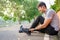 Exercise Injury Concept: A young Asian runner sits down on a park street due to pain in his ankle and grabs his sore ankle and
