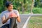 Exercise Injury Concept: A young Asian runner sits down on a park street due to pain in his knee and uses a hand to grasp the sore