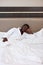 Exhausted afro man in bathrobe on bed in hotel