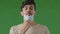 Exhausted arab brunet man indian hispanic guy stands isolated in green studio takes off respiratory medical face mask