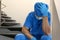 Exhausted doctor sitting on stairs indoors. Stress of health care workers during COVID-19 pandemic