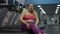 Exhausted obese Caucasian woman stretching tired legs sitting on treadmill in gym. Portrait of plus-size overweight lady