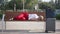 Exhausted tired Caucasian businesswoman falling asleep on bench in city with luggage. Wide shot of overwhelmed beautiful