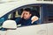 Exhausted young man sitting behind the steering wheel of the examination car showing thumb down gesture failed the driver license