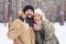 Exhilarated husband with thumb up hugging wife during the snowfall in the forest