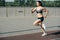 Exhilarated woman running fast outdoors on the track next to pavement sidewalk