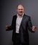 Exited bald business man in black suit showing the hands success winner sign on grey background. Closeup