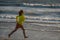 Exited carefree little boy running on wet coast near waving sea on sunny summer day. Kid running at summer beach