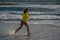 Exited carefree little boy running on wet coast near waving sea on sunny summer day. Kid running at summer beach
