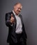 Exited comic bald business man in black suit showing the finger success thumb up sign on grey background. Closeup